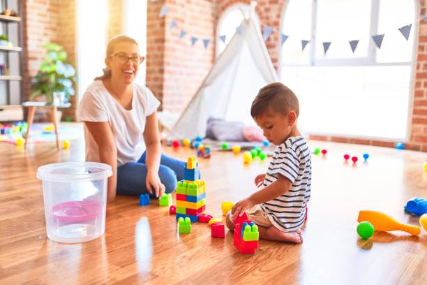 istock Beautiful teacher and toddler boy playing with construction blocks bulding tower at kindergarten 1185932607