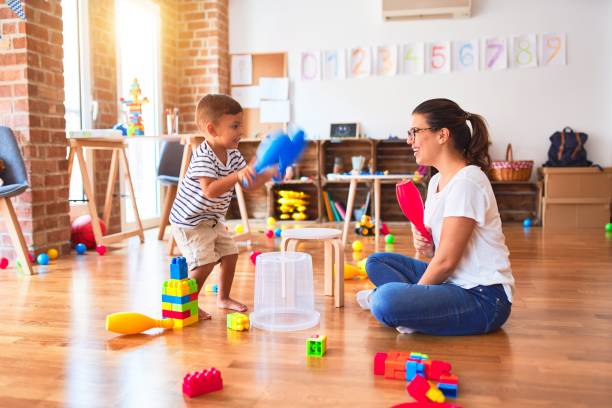 istock Beautiful teacher and toddler boy playing drum using skitlle and plastic basket at kindergarten 1185933155