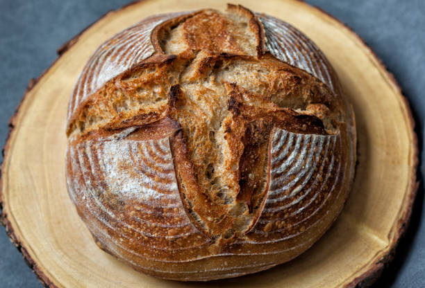 pan artesanal de pan tradicional de masa fermentada casera boule con corteza sobre una tabla de madera con fondo gris - enzo fotografías e imágenes de stock