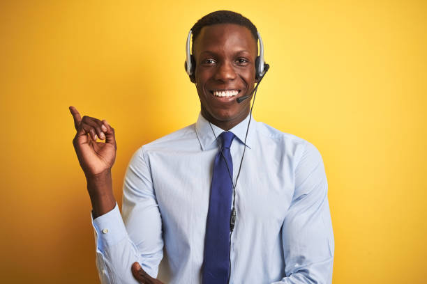 istock African american operator man working using headset over isolated yellow background with a big smile on face, pointing with hand and finger to the side looking at the camera. 1185936741