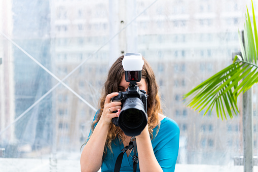 One young wedding photographer woman girl covering face with camera external flash taking picture photo looking at display and lens