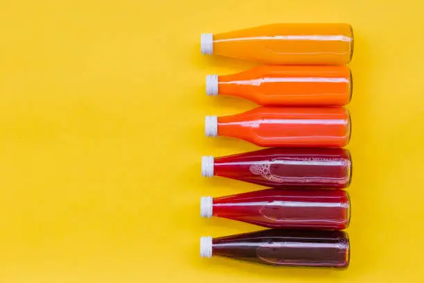 Photo of Juice Bottle Mock-Up, gradient juice bottles on yellow background. Variety of colorful Smoothies, top view. Healthy Food concept