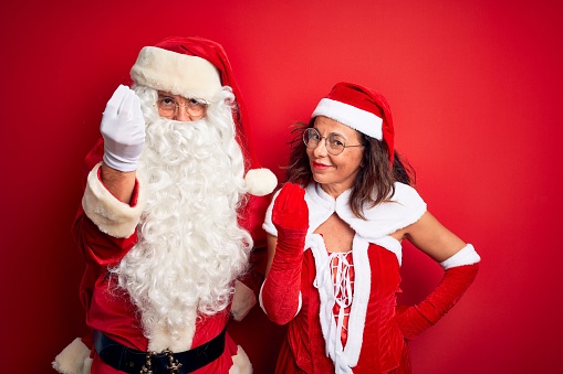 Middle age couple wearing Santa costume and glasses over isolated red background Doing Italian gesture with hand and fingers confident expression
