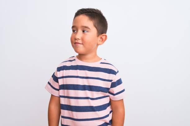 beau garçon d'enfant utilisant le t-shirt rayé occasionnel restant au-dessus du fond blanc d'isolement souriant regardant au côté et regardant loin pensant. - one person staring people smart casual photos et images de collection