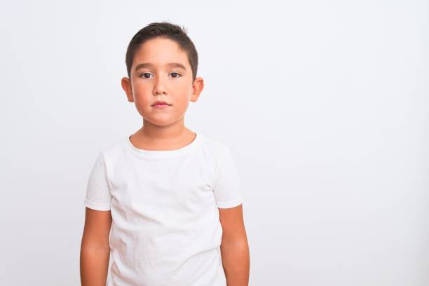 hermoso niño con camiseta casual de pie sobre fondo blanco aislado relajado con expresión seria en la cara. mirando la cámara de aspecto sencillo y natural. - t shirt child white portrait fotografías e imágenes de stock