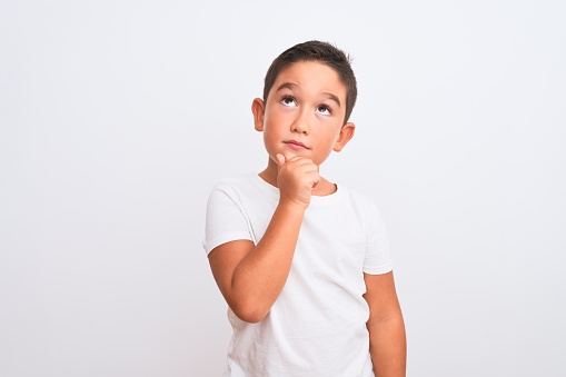Beautiful kid boy wearing casual t-shirt standing over isolated white background with hand on chin thinking about question, pensive expression. Smiling with thoughtful face. Doubt concept.