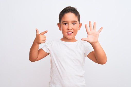 Beautiful kid boy wearing casual t-shirt standing over isolated white background showing and pointing up with fingers number seven while smiling confident and happy.