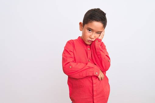 Beautiful kid boy wearing elegant red shirt standing over isolated white background thinking looking tired and bored with depression problems with crossed arms.
