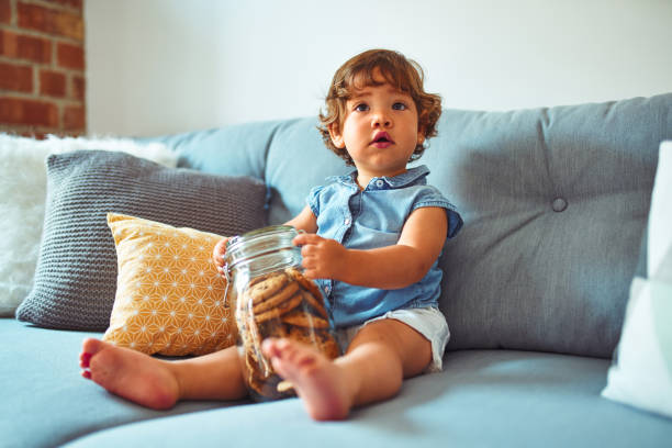 Beautiful toddler child girl holding jar of cookies sitting on the sofa Beautiful toddler child girl holding jar of cookies sitting on the sofa preschooler caucasian one person part of stock pictures, royalty-free photos & images