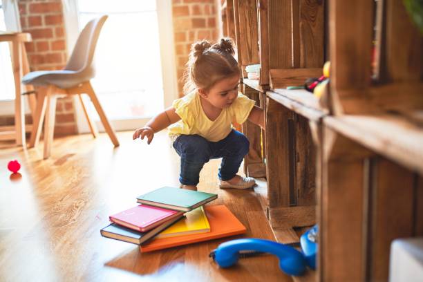 Beautiful toddler taking books of shelving at kindergarten Beautiful toddler taking books of shelving at kindergarten montessori education photos stock pictures, royalty-free photos & images