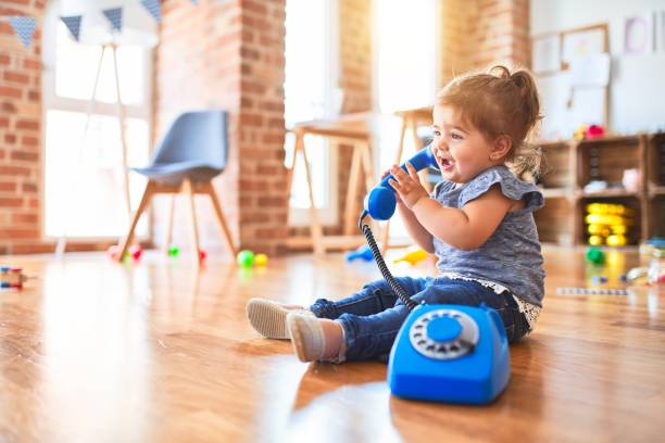 Beautiful toddler sitting on the floor playing with vintage phone at kindergarten Beautiful toddler sitting on the floor playing with vintage phone at kindergarten language learning in babies stock pictures, royalty-free photos & images