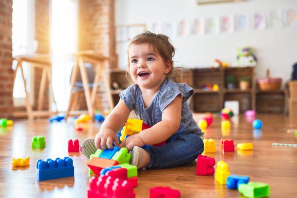 Beautiful toddler sitting on the floor playing with building blocks toys at kindergarten Beautiful toddler sitting on the floor playing with building blocks toys at kindergarten toy block photos stock pictures, royalty-free photos & images