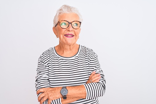 Mujer de pelo gris mayor con gafas de camiseta azul a rayas de color marino sobre fondo blanco aislado sonriendo mirando hacia un lado y mirando hacia fuera pensando. photo