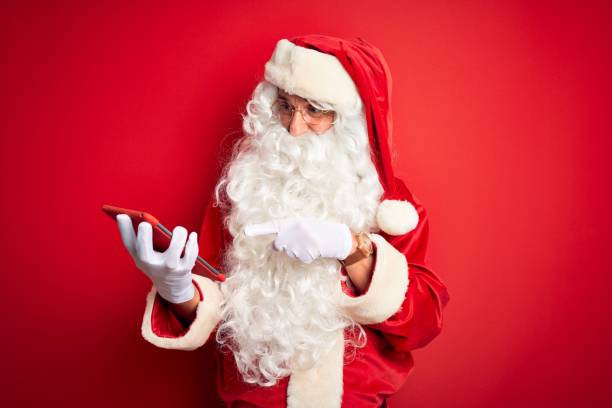 istock Middle age man wearing Santa Claus costume using tablet over isolated red background very happy pointing with hand and finger 1185948763