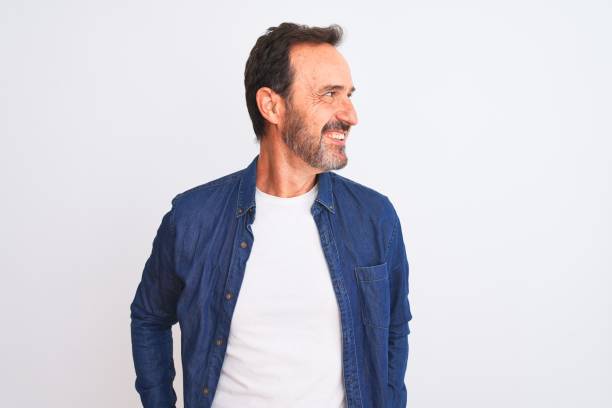 istock Middle age handsome man wearing blue denim shirt standing over isolated white background looking away to side with smile on face, natural expression. Laughing confident. 1185950328