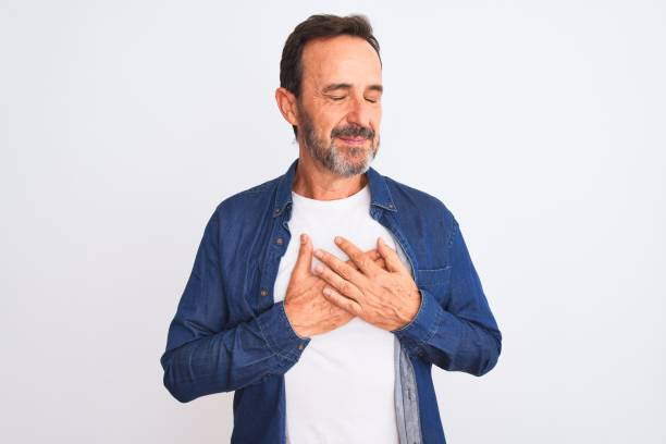 istock Middle age handsome man wearing blue denim shirt standing over isolated white background smiling with hands on chest with closed eyes and grateful gesture on face. Health concept. 1185950351