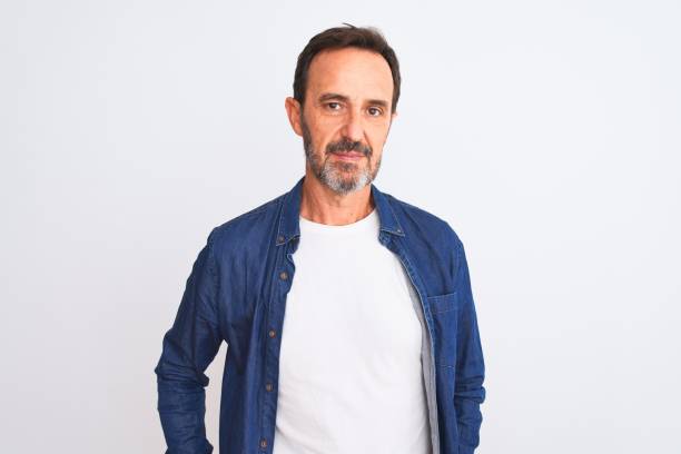 Middle age handsome man wearing blue denim shirt standing over isolated white background Relaxed with serious expression on face. Simple and natural looking at the camera.