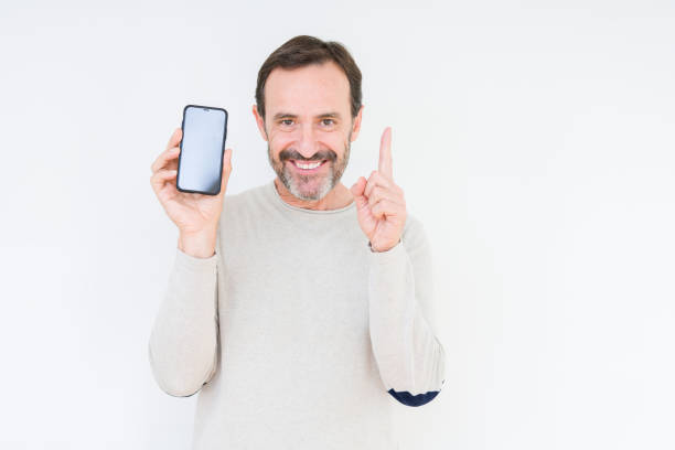 istock Senior man showing smartphone screen over isolated background surprised with an idea or question pointing finger with happy face, number one 1185952034