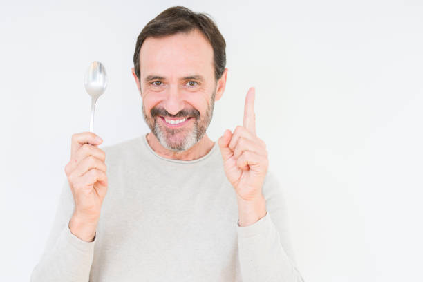 istock Senior man holding silver spoon over isolated background surprised with an idea or question pointing finger with happy face, number one 1185952327
