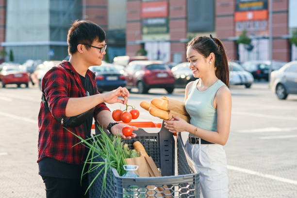 Beautiful young asian couple checking purchased food in the shopping cart near the big store Young asian couple checking their shopping cart full of healthy organic food on the background of big store. Healthy food concept. vietnamese girls for sale stock pictures, royalty-free photos & images