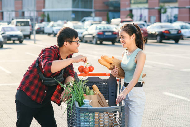 Beautiful young asian couple checking purchased food in the shopping cart near the big store Young asian couple checking their shopping cart full of healthy organic food on the background of big store. Healthy food concept. vietnamese girls for sale stock pictures, royalty-free photos & images