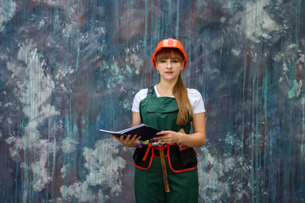 istock Woman worker in coverall with tool belt posing near grey wall 1185959957