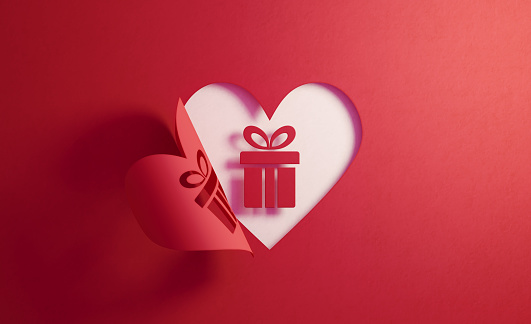 Gift box icon inside of a red folding heart shape on white background. Horizontal composition with  copy space. Gift concept.