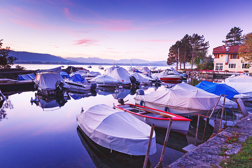 Colorful autumnal scenery of Yacht club at Geneva lake during fascinating sunrise in Switzerland. Beautiful small cozy bay with sheathed recreation boats. Traditional view of lake Geneva. Violet color