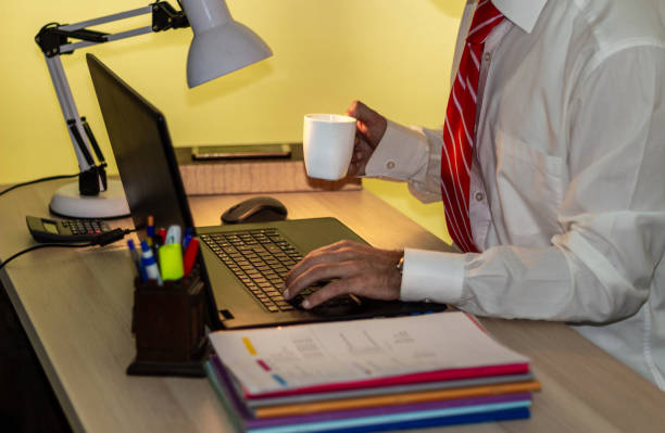 o homem no terno trabalha com portátil no escritório e bebe o café. o homem de negócios na camisa branca com laço vermelho trabalha - shirt and tie typing communication part of - fotografias e filmes do acervo