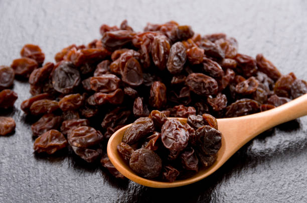 istock Raisins in wooden spoon on black stone background 1185980171