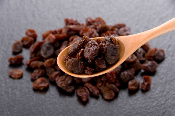 istock Raisins in wooden spoon on black stone background 1185981434