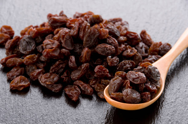 istock Raisins in wooden spoon on black stone background 1185983121