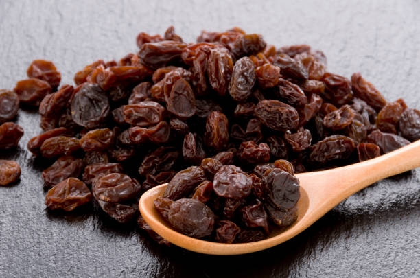 istock Raisins in wooden spoon on black stone background 1185983130