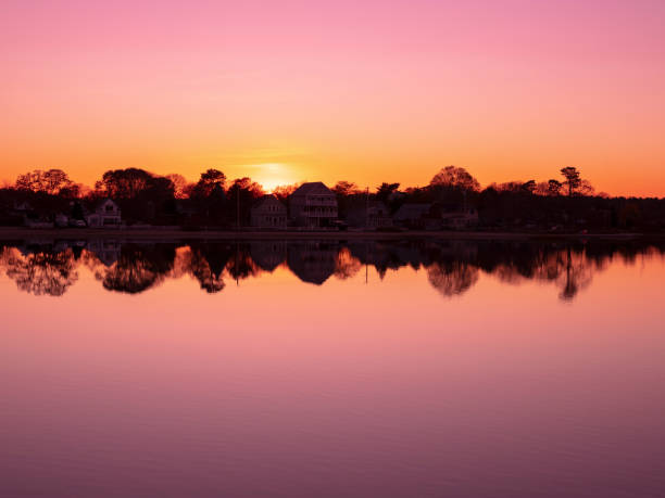 Symmetrical reflected shoreline houses in silhouette dividing a pink gradient sky and calm lake water horizontally at the horizon
