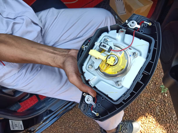 the technician in uniform holding the airbag panel that take off from the steering wheel in passenger cabin of the car between onsite service - airbag imagens e fotografias de stock