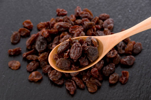 istock Raisins in wooden spoon on black stone background 1185997198
