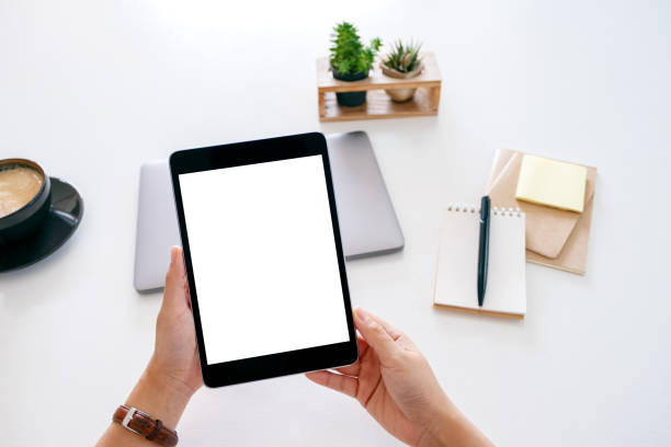 istock hands holding a tablet with blank white screen and laptop computer on wooden table in office 1185998013