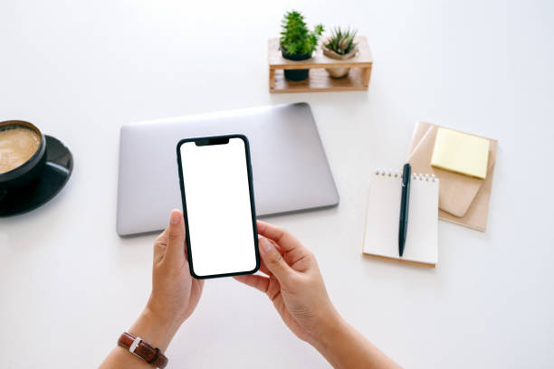 istock hands holding mobile phone with blank screen and laptop computer on the table in office 1185998037