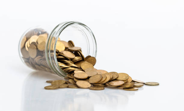 istock Coins spilling from a glass jar on white background 1186018871