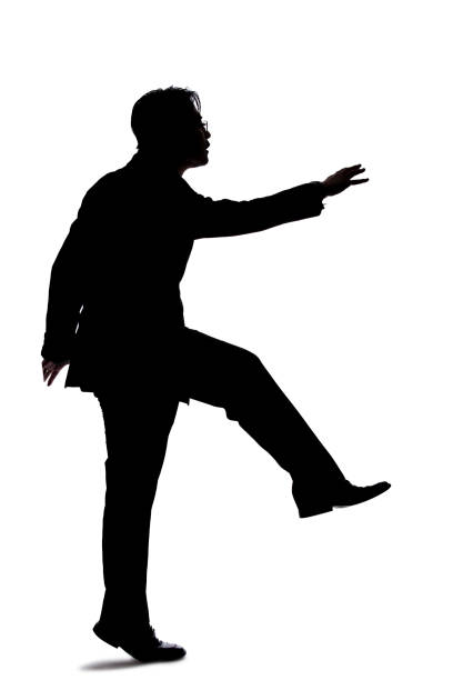 Silhouette of a backlit model posing as a businessman on a white background.  He is jumping up or leaping forward.