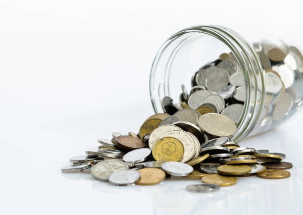 istock Coins spilling from a glass jar on white background 1186019586