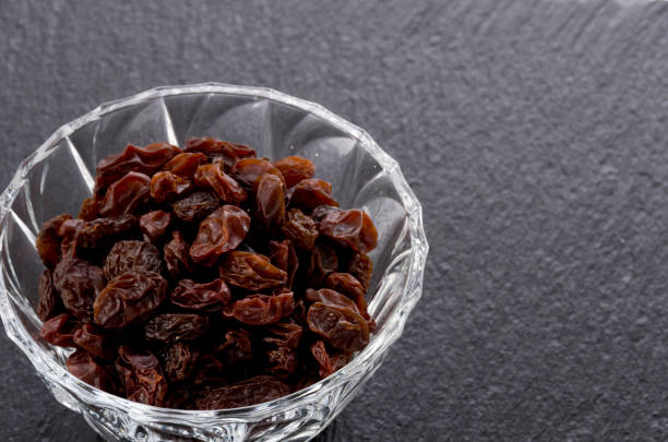 Raisins in Glass bowl on black stone background