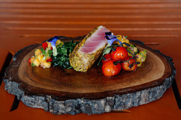 Roasted Tuna Steaks Crusted with Herbs and grilled vegetable and mango salsa on wood plate - close up fine dining food shot.