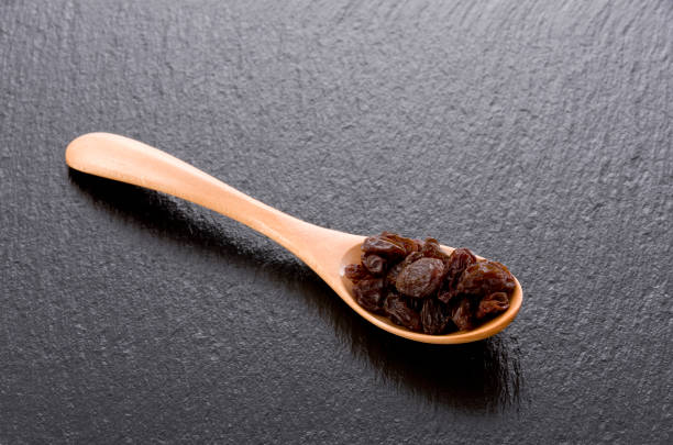 Raisins in a wooden spoon on black stone background