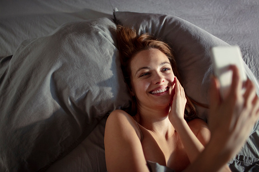 Close up of a young woman using her phone while lying in bed