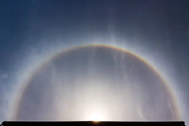 Photo of Fantastic beautiful sun halo phenomenon or sun with circular rainbow and fluffy altocumulus clouds over the skyscraper.