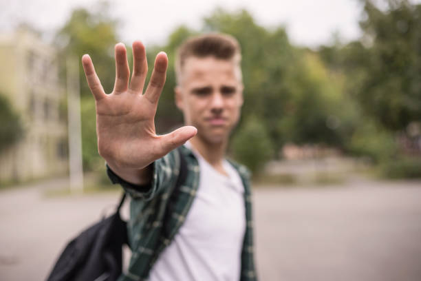 Frustrated teenager putting his hand Serious teenage boy gesturing stop sing with his hand and saying 'stop to violence!' with body language self defense stock pictures, royalty-free photos & images