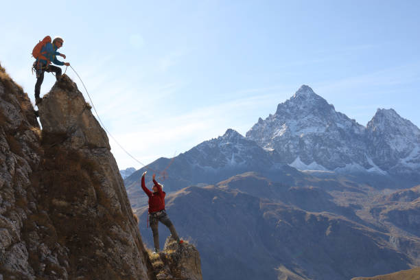 istock Mountaineer throws rope to partner from mountain summit 1186041945