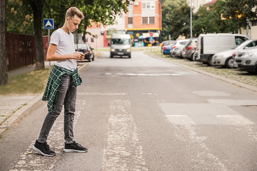 Niño cruzando la calle en un paso de peatones y escuchando música en su teléfono celular photo