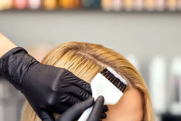 Hands in black gloves are painting the female hair with brush in a white color close up.